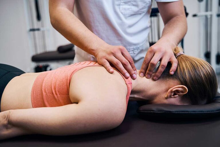 A chiropractor explaining spinal alignment using a model spine to a patient in an exam room.