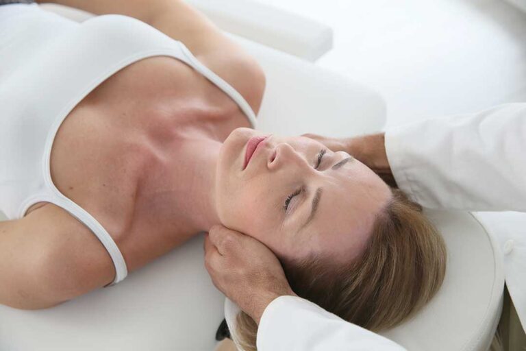 A person lying on their side in bed with a pillow between their knees and head supported by a pillow.