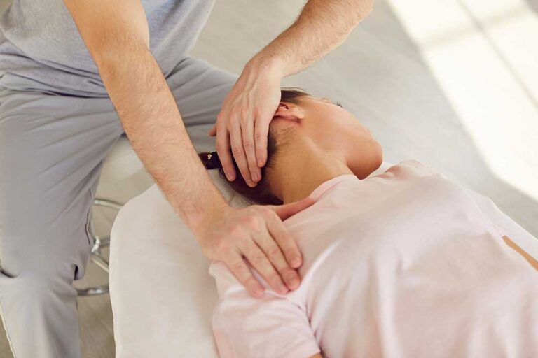 A person sitting on a couch holding their neck with one hand, looking uncomfortable after a minor accident.